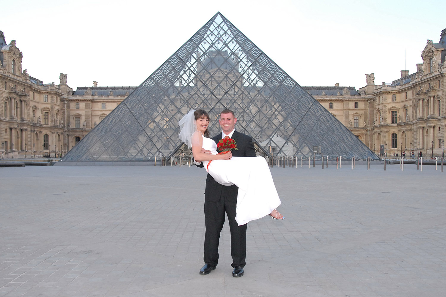 Mariée dans les bras du marié devant la pyramide du Louvre, Paris.