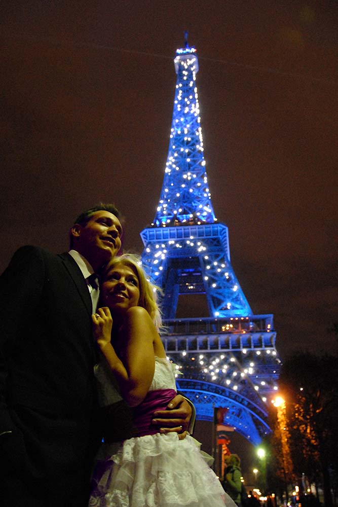 Mariage - Couple de mariés devant la tour Eiffel bleue étincelant dans la nuit.